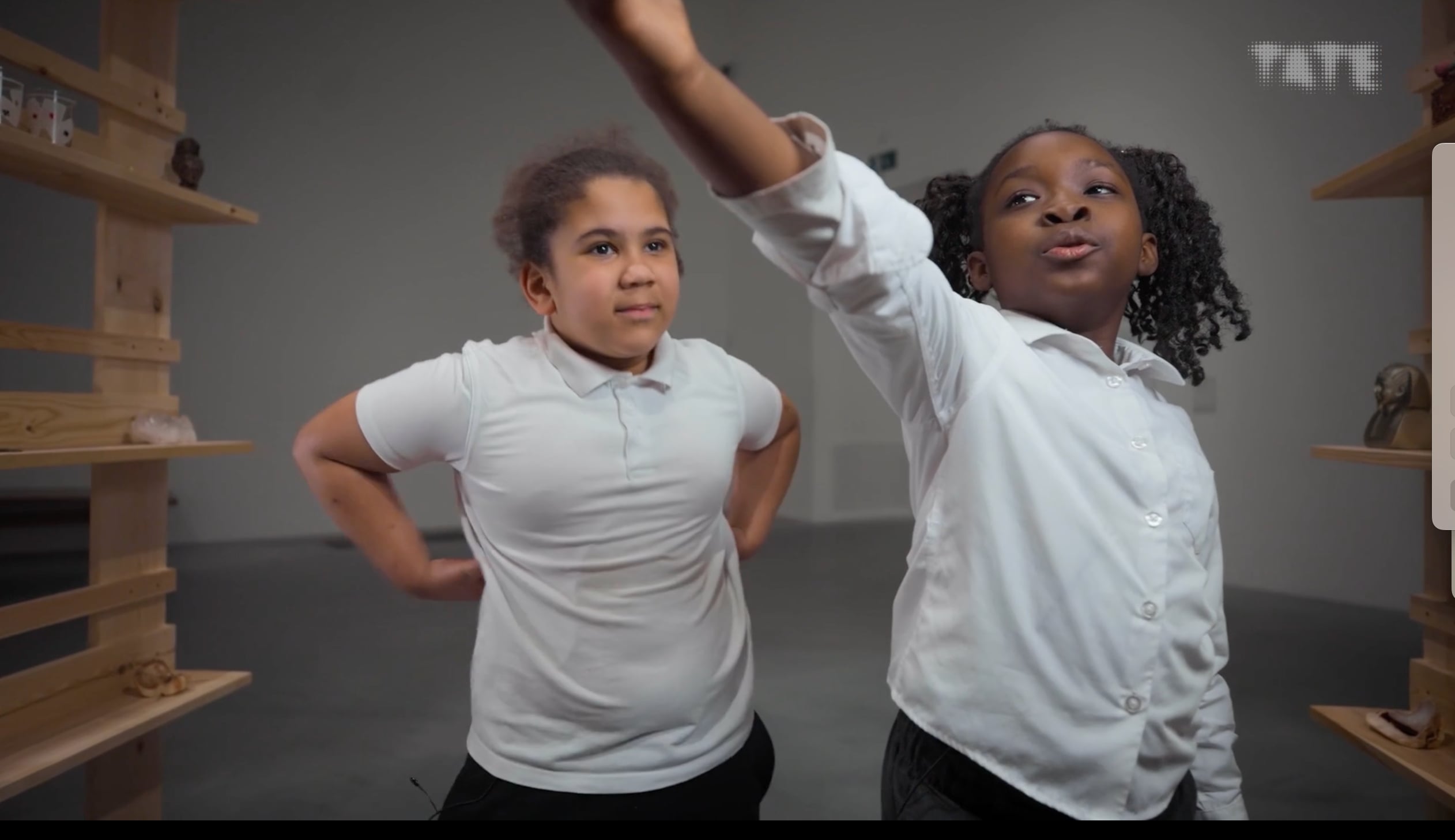 Two children in white school shirts point at things off camera